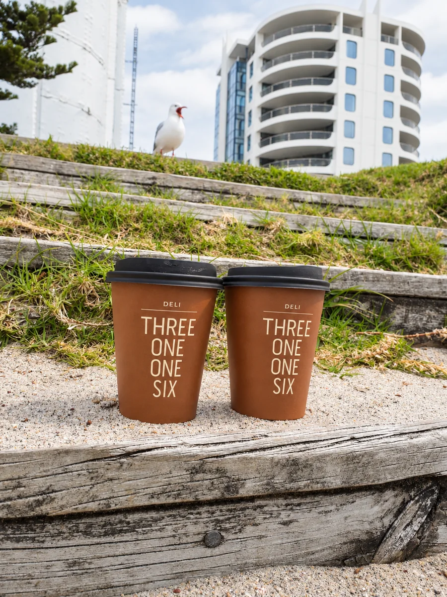 Two branded Three One One Six takeaway cups near the beach